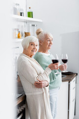 happy retired women holding glasses with wine in kitchen