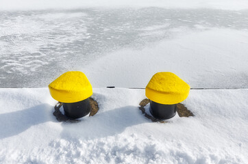 Mooring bollards on a pier by a frozen river.