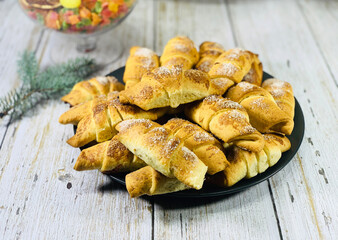 Bagel cookies lie on the table. Mini croissants with filling. Candied fruits in a vase in the background. Muffin sprinkled with sugar.