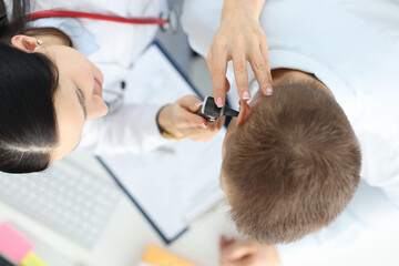 Otorhinolaryngologist examining patient with otoscope top view closeup