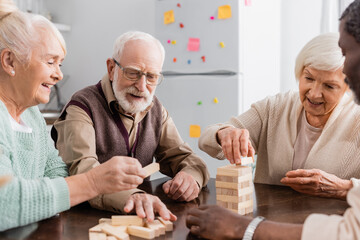 happy interracial pensioners smiling while playing tower wood blocks game at home