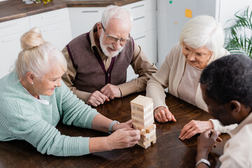 high angle view of happy multicultural pensioners playing tower wood blocks game at home