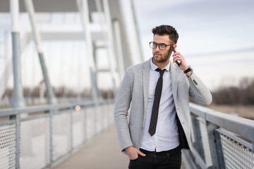 Young businessman standing on the bridge and talking on smartphone. Yuppie outdoors relaxing