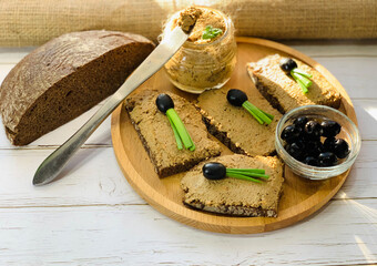 Cooked pate spread on black bread. Loaf of black bread on burlap. Liver pate in a glass jar.