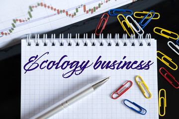 On the desktop are a forex chart, paper clips, a pen and a notebook in which it is written - Ecology business