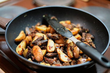 Frying pan with fried golden potatoes and pieces of pork with lots of spices.