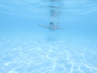 Fototapeta premium Boy swimming under blue water in pool