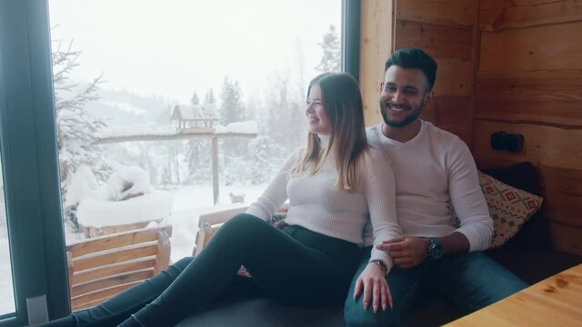 Multiracial couple enjoying winter holidays. Huggin near the window and watching snow. High quality 4k footage
