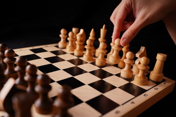 Close up of white and black wooden chess pieces on board. Woman's hand makes first move of white pawn on chessboard. Concept of intelligent, logical and strategic game.