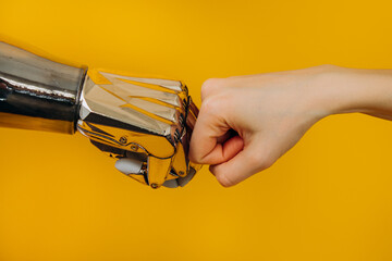 Bionic robot arm and the human arm are knocking fists, a greeting sign on a bright yellow...