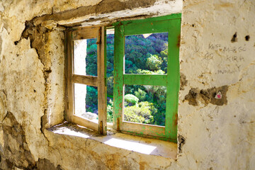 Old wooden window frame and wall in a ruin overlooking the nature in tenerife. The colors are brown green on the frame and beige on the wall. Outside Los gigantes, Tenerife / Spain