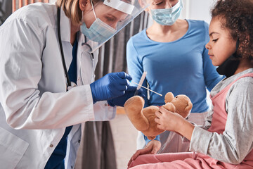 Doctor and little girl playing, while treating teddy bear
