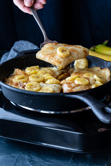 Cast iron skillet with Banana Foster and crepes cooking against a black background.