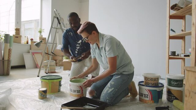 Caucasian woman pouring paint into tray while renovating home together with Afro-American husband