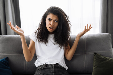 Smiling multiracial black curly girl uses cell phone, talking with friends or family while sits on...