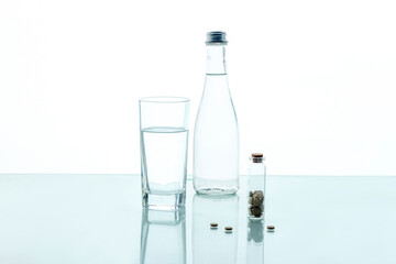 Pills in a transparent jar with a glass of water and a glass bottle on a white background. Medical concept.