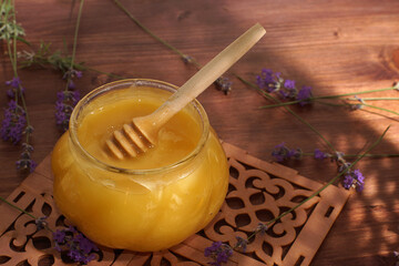 A jar of natural honey with a spindle spoon on a mat on the table next to lavender