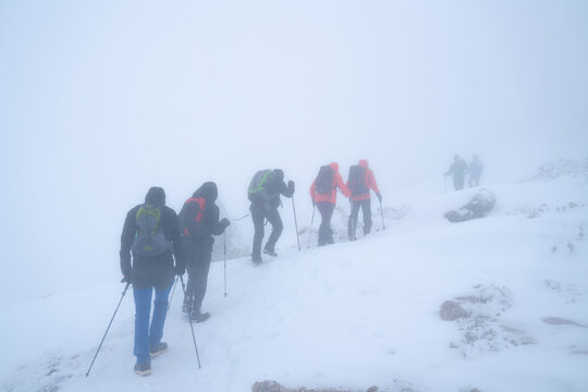 IMAGE OF A GROUP OF PEOPLE HIKING IN EXTREME CONDITIONS. ALPINISTS TREKKING IN HARSH WINTER CONDITIONS. COLD AND BAD WEATHER CONCEPT.