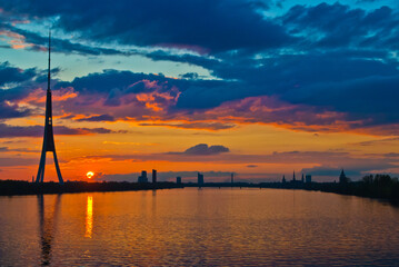 sunset. in the photo, the clouds are illuminated by the evening sun,in the foreground is a river, in the background is a city