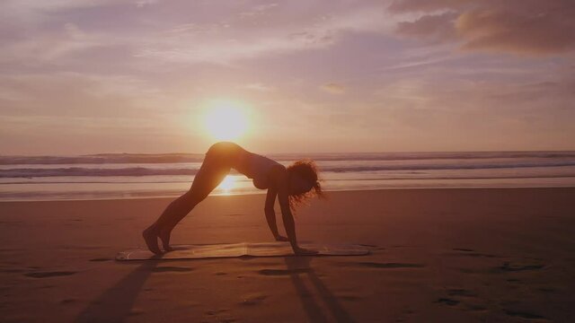 A girl practices yoga on the beach at sunset