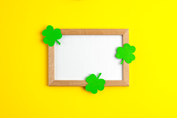 Green paper clovers flat lay top view on wooden frame in the centre with white copy space on yellow background Saint Patrick's Day 17 march traditional spring celebration holiday and good luck concept
