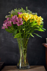 Blooming bouquet of colourful vibrant flowers in a clear vase against a black background. 