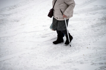 Closeup of old woman walking in the street with stick by snowy day