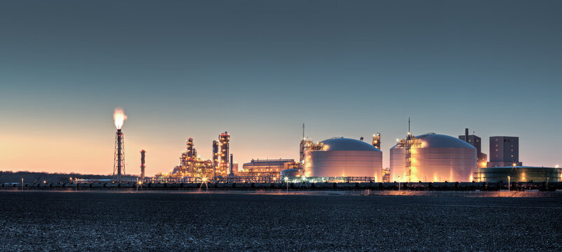 Fertilizer plant in an agricultural landscape at sunset. 
Railroad tanker cars stretched across the image. 