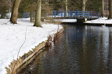 Fototapeta premium Snowy winter landscape with trees and canal, in the city park. 