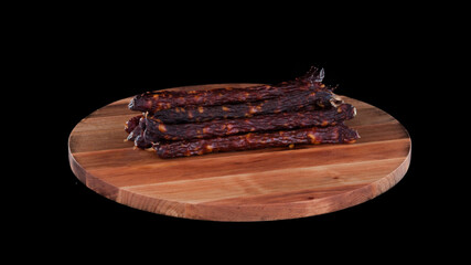 Meat raw smoked sausage on wooden round board on black isolated background, several sticks and pieces