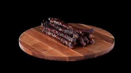 Meat raw smoked sausage on wooden round board on black isolated background, several sticks and pieces