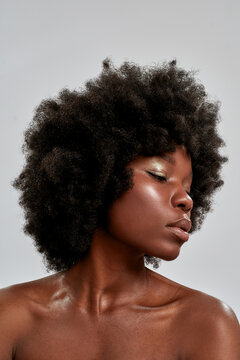 Portrait of beautiful african american female model with afro hair and perfect smooth glowing skin looking down, posing isolated over gray background