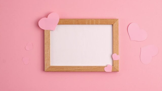 Stop motion animation of pink paper hearts on and near wooden frame on pink background at the centre side Valentine's day romantic anniversary wedding holiday concepts Flat lay with copy space