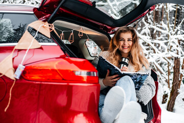 Fototapeta na wymiar winter romance concept car travel in winter, in red car drinks hot tea from a thermos, picnic in a frosty winter forest, valentine