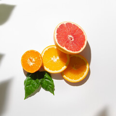 Creative composition with fresh tropical fruit. Tangerine, orange, grapefruit and green leaves arranged on white background. Natural concept. Minimal flat lay.