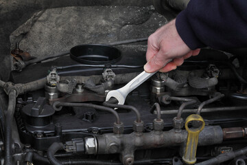 Car mechanic worker fixing modern common rail diesel engine, closeup of hand with spanner tool, rail, pipeline and injectors