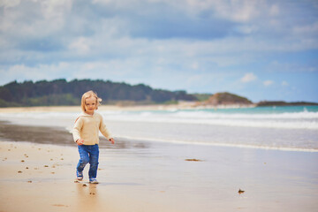 Fototapeta na wymiar Adorable toddler girl on the sand beach at Atlantic coast of Brittany, France