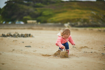 Adorable toddler girl playing with stones and building a town on the sand beach