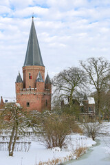 Fototapeta na wymiar Snow white winter wonderland with pointy rooftop tower with cants of Drogenapstoren part of historic city center of medieval Hanseatic town during a snowstorm