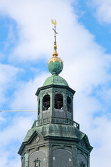 Highest top of the Walburgiskerk tower with a golden ornament against a blue sky and wave pattern clouds