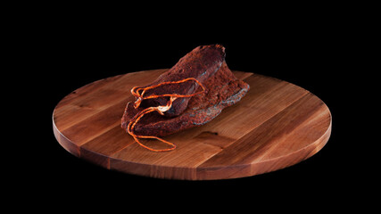 Meat raw smoked sausage on wooden round board on black isolated background, several sticks and pieces