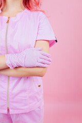Croped portrait of attractive pink-haired female doctor wearing safety pink uniform crossing arms contamination prevention isolated pink pastel color background