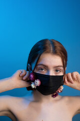 Girl posing in a studio in a black mask with flowers