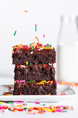 homemade chocolate frosted brownies with rainbow colored sprinkles on a white background