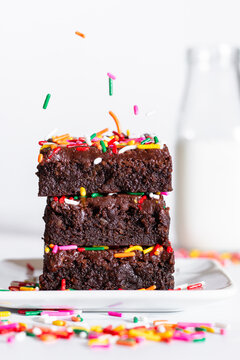 homemade chocolate frosted brownies with rainbow colored sprinkles on a white background