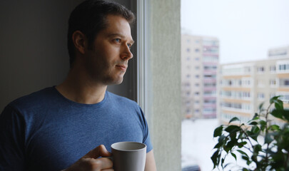 Man with cup of tea looks out the window.
