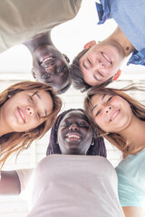 Upward view of teenagers smiling together in a circle. Multi ethnic friends happy, freindship and...