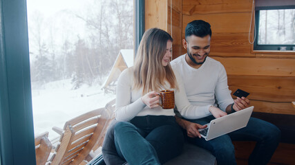 Happy young multiracial couple using credit card to do online shopping. Booking winter vacation....
