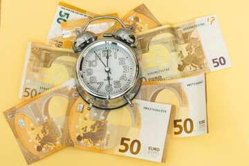 horizontal photo of a background of fifty euro banknotes and an analogical clock as time money work