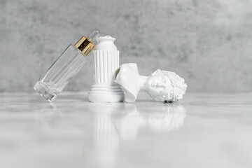 Transparent cosmetic serum in a pipette bottle on a gray concrete-marble background. Next to it is a white plaster bust of a woman. The concept of care and destruction